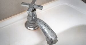 Hard water stain removal in Austin: Close-up of a chrome bathroom faucet covered in severe white mineral deposits and scaling.